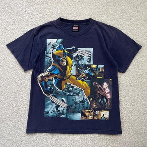 May include: Navy blue t-shirt featuring a graphic of Wolverine from Marvel Comics. The design shows Wolverine in action with his claws extended, set against a backdrop of comic book panels. The Marvel logo is visible.