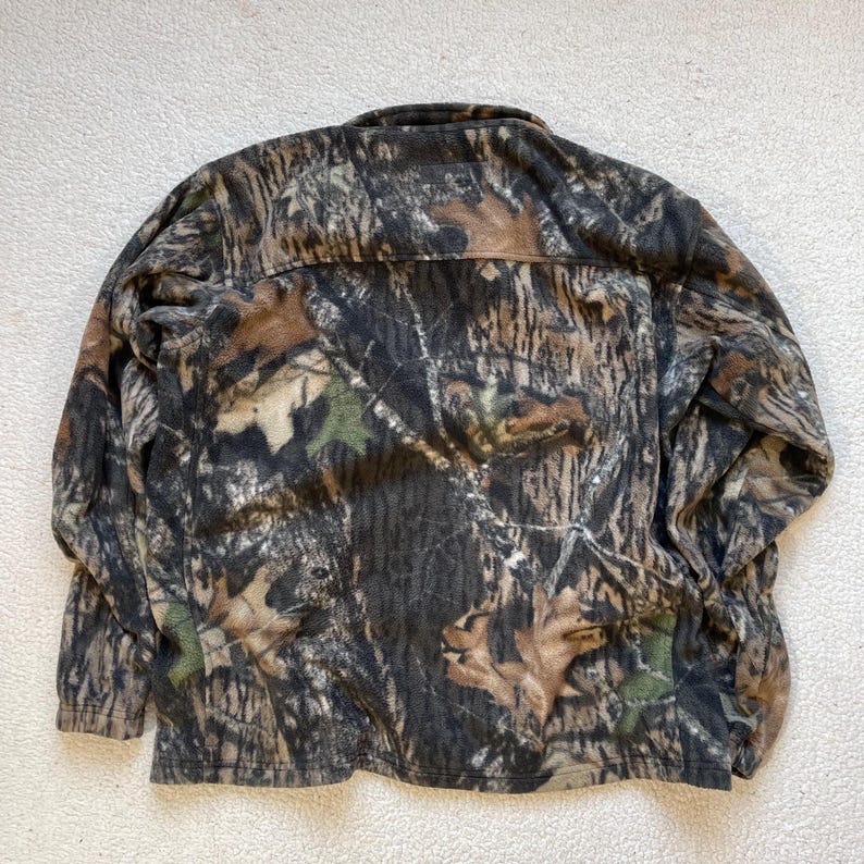 May include: A brown, green, and tan camouflage fleece jacket with a zipper closure.