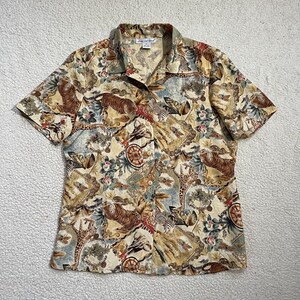 Op de afbeelding: Korte mouwen button-down shirt met een safari dierenprint. Het shirt heeft tijgers, zebra's, giraffen en andere dieren in een beige, bruin en blauw kleurenpalet. Het shirt heeft een kraag en een knoopsluiting.