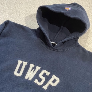 May include: A navy blue hooded sweatshirt featuring the white text UWSP across the chest. The hood includes a small embroidered purple and gold logo detail at the top center. The garment is constructed with a drawstring-free hood and long sleeves.
