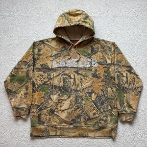 Vintage 00s Cabela’s Realtree Camo Hoodie Carpet Logo Stitched Boxy Outdoor Hooded Pullover Sweatshirt Mens L