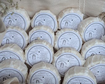 May include: A collection of round, white, natural shampoo bars wrapped in white paper. Each bar has a label with the name of the scent, "Maple's Milk", and a list of ingredients. The scents include Tea Tree, Lemongrass, Honeysuckle, Peppermint Vanilla, Lavender Rosemary, and more.
