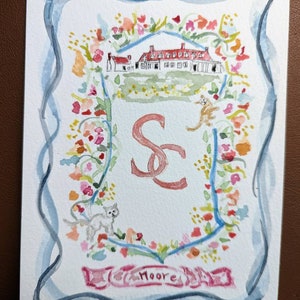 Könnte beinhalten: Aquarellmalerei eines Wappens mit einem Haus, Blumen und den Initialen "S & E" in rosa und roter Schrift. Das Wort "Moore" ist in rosa Schrift am unteren Rand des Wappens geschrieben.