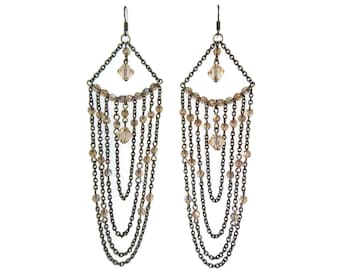 May include: A pair of chandelier earrings with a geometric design. The earrings feature a dark metal chain frame with dangling chains and small, round, amber-colored beads. A larger crystal-like bead is at the top of each earring.
