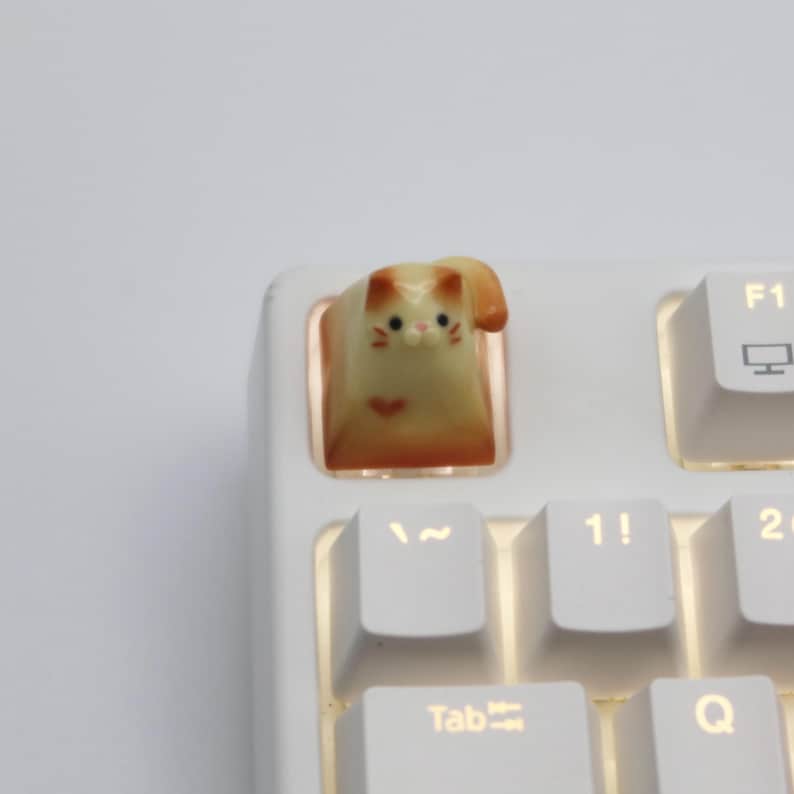 May include: A white keyboard with a small, light yellow and orange cat figurine keycap on the "~" key.
