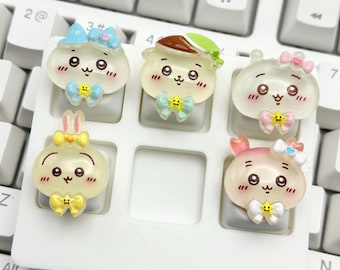 May include: A set of six custom keycaps with adorable cartoon character designs. Each keycap features a different character with a unique bow and facial expression. The keycaps are in various pastel colors and are designed to fit on a standard keyboard.