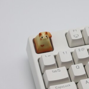 May include: A white keyboard with a cat-shaped keycap. The keycap is orange and white and has a cute face.