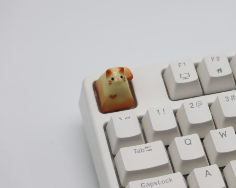 May include: A white keyboard with a cat-shaped keycap. The keycap is orange and white and has a cute face.