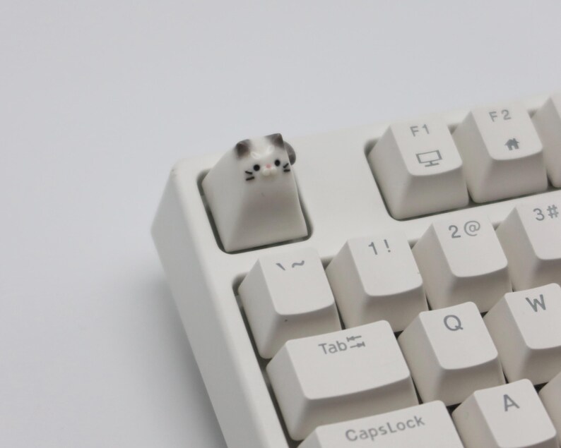 May include: White mechanical keyboard with a cat-shaped keycap. The keycap is white with black eyes and a gray nose. The keyboard has keys labeled with letters, numbers, and symbols.