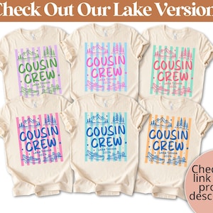 Op de afbeelding: Zes cr&egrave;mekleurige t-shirts met een afbeelding van verticale strepen, bergen, bomen, een kano en een steiger. De tekst luidt COUSIN CREW Lake Tahoe 2026. De kleuren van de afbeelding vari&euml;ren per shirt, met groene, roze, turquoise, blauwe en oranje accenten.