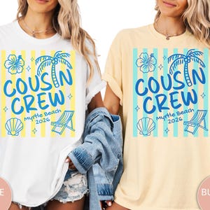Op de afbeelding: Twee T-shirts met korte mouwen, &eacute;&eacute;n wit en &eacute;&eacute;n botergeel, elk voorzien van een blauwe grafische print met verticale strepen, een palmboom, een hibiscusbloem, een schelp, een strandstoel en de tekst "COUSIN CREW Myrtle Beach 2026".