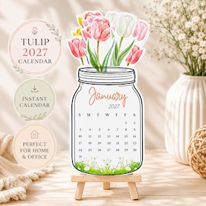 Può includere: Un calendario 2027 a forma di barattolo di vetro riempito con tulipani rosa, bianchi e gialli. Il calendario mostra il mese di gennaio 2027 con una griglia di date e un'illustrazione di erba verde sul fondo. Poggia su un piccolo cavalletto in legno.