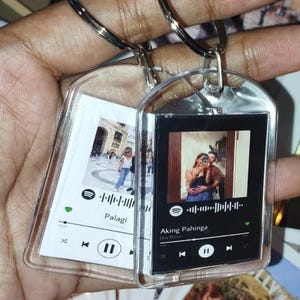 May include: Two clear acrylic keychains with silver key rings. One keychain features a photo and the word "Palagi" with a Spotify interface. The other keychain displays a photo and the song "Aking Pahinga" by Dito Perez.