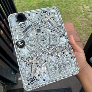 May include: A rectangular, silver-toned decorative item with the word "GOD" and "DAD" spelled out in sparkling embellishments. The design includes crosses, chains, and black accents. A black pom-pom and other decorative elements complete the design.