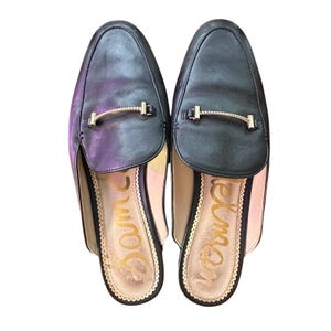 May include: A pair of black leather slip-on shoes with a gold chain detail. The shoes have a pointed toe and a low heel. The brand name "Sam Edelman" is visible on the insole.