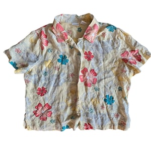 May include: A yellow short-sleeved button-down shirt with a floral print in shades of red, pink, blue, and yellow.