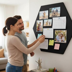 Könnte beinhalten: Eine große schwarze, sechseckige Pinnwand zur Wandmontage mit mehreren Familienfotos, zwei Monatskalenderblättern mit der Aufschrift Family Plan und bunten Haftnotizen, die mit kleinen Reißzwecken auf der dunklen Oberfläche befestigt sind.