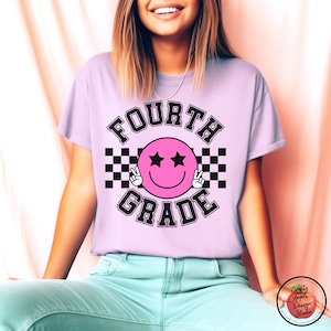 May include: A light purple t-shirt with the text "FOURTH GRADE" in black letters. A pink smiley face with black eyes and peace signs is in the center of the text. The smiley face is surrounded by a black and white checkered pattern.
