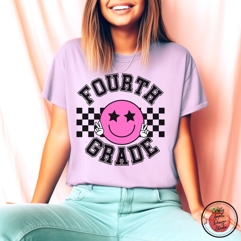 May include: A light purple t-shirt with the text "FOURTH GRADE" in black letters. A pink smiley face with black eyes and peace signs is in the center of the text. The smiley face is surrounded by a black and white checkered pattern.