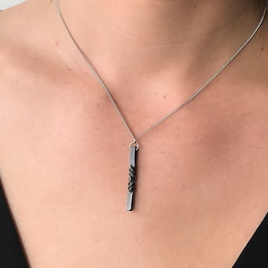 May include: A silver chain necklace with a twisted black metal pendant.