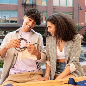 Smiling couple looking at iron anniversary belt buckle he has just been gifted in an outdoor, coffee shop city setting.