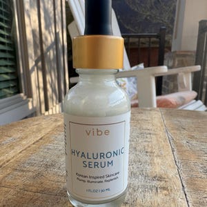 Peut inclure: Flacon en verre transparent de s&eacute;rum &agrave; l'acide hyaluronique avec compte-gouttes noir et bouchon dor&eacute;. L'&eacute;tiquette indique "vibe HYALURONIC SERUM Korean Inspired Skincare". Le flacon contient 30 ml de s&eacute;rum.