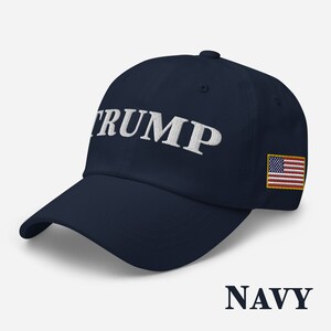 May include: A navy blue baseball cap with the word "TRUMP" embroidered in white on the front. The cap also features a small American flag patch on the right side.