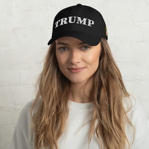 May include: A black baseball cap with the word "TRUMP" embroidered in white on the front. The cap has a small American flag patch on the side.