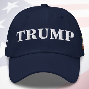 May include: A navy blue baseball cap with a white embroidered "TRUMP" on the front and a small American flag patch on the side.
