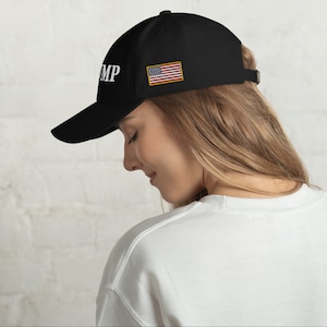 May include: Black baseball cap with a white "TRUMP" embroidered on the front and a small American flag patch on the side.
