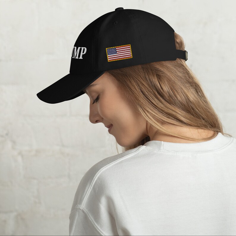 May include: Black baseball cap with a white "TRUMP" embroidered on the front and a small American flag patch on the side.