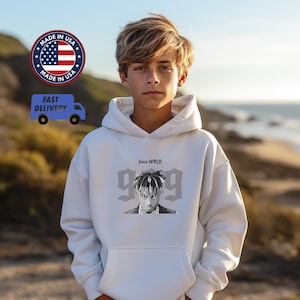 May include: A white hoodie featuring a black and white image of a person with the text "Juice WRLD" and the number "999". The hoodie has a front pocket and a hood. The image also includes a "Made in USA" logo and a "Fast Delivery" graphic.