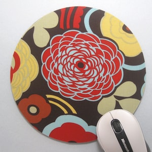 May include: A round brown mouse pad with a colorful floral design. The design features red, yellow, blue, and white flowers on a brown background.