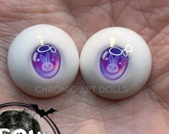 May include: Two white doll eyes with a purple and pink galaxy design and a bunny rabbit. The text "CHRONIC ART DOLLS" is printed on the eyes. The eyes are round and have a glossy finish.