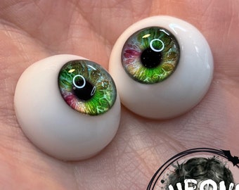Peut inclure: Deux yeux de poupée verts, roses et dorés avec des pupilles noires. Les yeux sont sur un fond blanc.