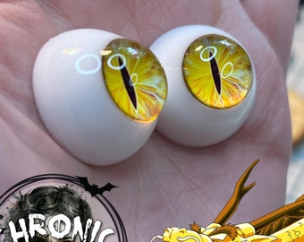 May include: A pair of yellow and orange glass eyes with black pupils. The eyes are round and have a glossy finish. The eyes are set against a white background.