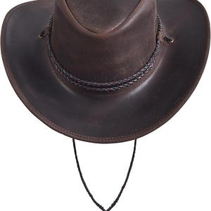 Puede incluir: Sombrero de vaquero de cuero marr&oacute;n con una banda trenzada alrededor de la corona y una correa para la barbilla. El sombrero tiene un ala ancha y un estilo occidental cl&aacute;sico. El sombrero est&aacute; hecho de cuero envejecido.