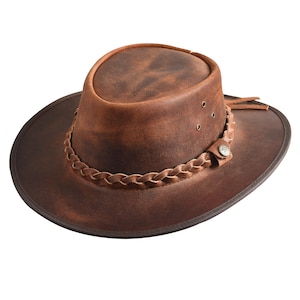May include: A brown leather hat with a wide brim and a braided leather band. The hat has a distressed finish and a small button detail on the side. The hat has a classic cowboy hat style.