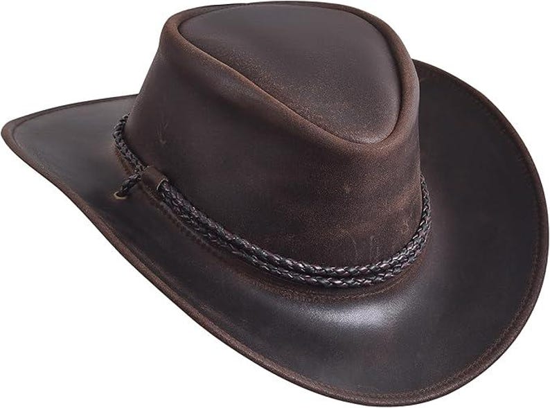 Puede incluir: Un sombrero de vaquero de cuero marr&oacute;n con ala ancha y una banda trenzada alrededor de la corona. El sombrero tiene un acabado envejecido, lo que le da un aspecto robusto y desgastado. El ala del sombrero mide unos 8,9 cm.