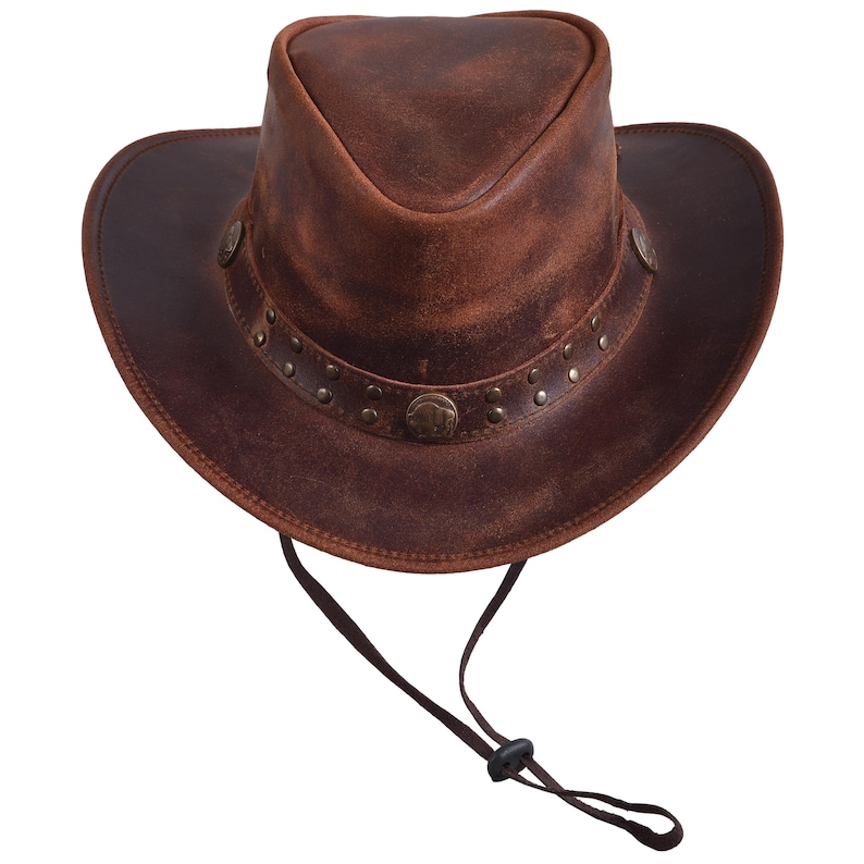 May include: A brown leather cowboy hat with a wide brim and a tall crown. The hat features a decorative band with metal studs and a chin strap. The hat is made of distressed leather and has a vintage look.