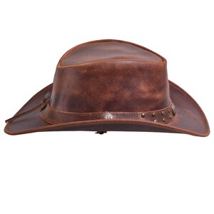 May include: A brown leather cowboy hat with a distressed finish. The hat features a wide brim, a tall crown, and decorative metal studs and conchos around the band. A leather cord is attached to the brim.