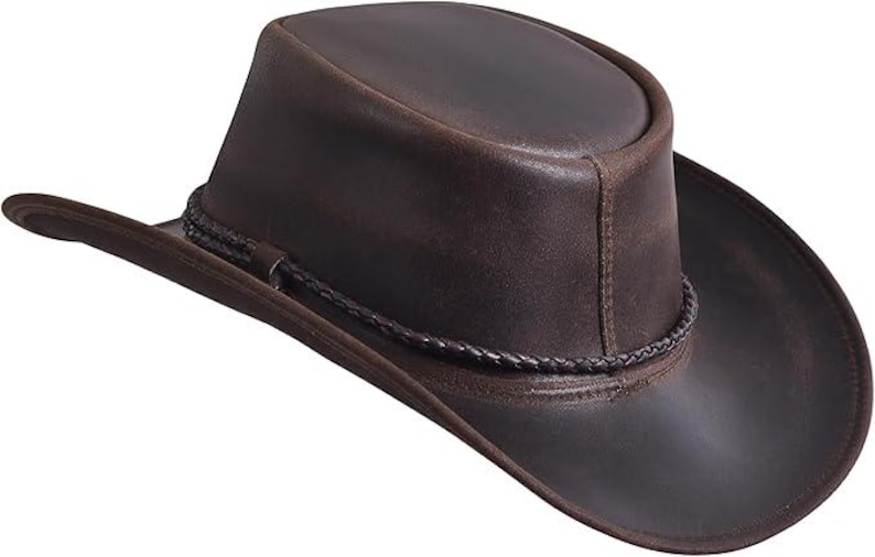 Puede incluir: Sombrero de vaquero de cuero marr&oacute;n con ala ligeramente curvada y banda trenzada alrededor de la corona. El sombrero tiene un acabado envejecido. Un sombrero de estilo western cl&aacute;sico.