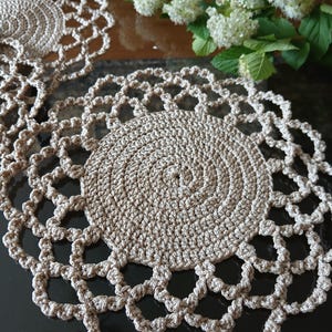 May include: Two crocheted beige doilies with a circular design and intricate lace edging.