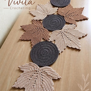 Pode incluir: Um caminho de mesa composto por formas de folhas de bordo e tapetes circulares de crochê em tons de bege, castanho e cinzento escuro. O arranjo apresenta motivos alternados de folhas e círculos. O texto Vivita Crocheting é visível no canto superior esquerdo.
