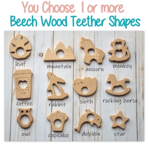May include: A set of 12 wooden teether shapes for babies, including a leaf, mountain, unicorn, monkey, coffee cup, rabbit, sloth, rocking horse, owl, cupcake, dolphin, and star. The teethers are made of natural beech wood and are unpainted.