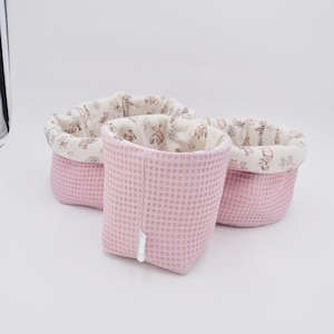 Op de afbeelding: Drie roze opbergmanden van wafelweefsel. De manden hebben een voering van stof met een patroon van teddyberen en andere dieren. De manden zijn verschillend van grootte en zijn in elkaar genest.