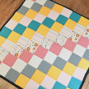 Könnte beinhalten: Ein Patchwork-Quilt mit verschiedenen gemusterten Quadraten in Gelb, Türkis, Rot, Weiß und Marineblau. Der Quilt hat Punkte, Streifen, Vichy-Karo und Tiermuster. Der Quilt hat eine schwarze Umrandung.