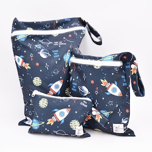 Pode incluir: Três sacos húmidos reutilizáveis com tema espacial. O saco maior é azul com estrelas e planetas brancos, foguetes e o texto "Out of this world". O saco médio é azul com estrelas e planetas brancos, foguetes e o texto "Over the moon". O saco menor é azul com estrelas e planetas brancos, foguetes e o texto "Fun space".