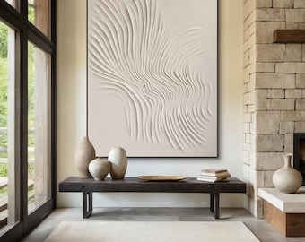 Puede incluir: Una pintura abstracta blanca con un diseño texturizado en relieve de líneas y curvas. La pintura está enmarcada en negro y cuelga de una pared blanca sobre un banco de madera.