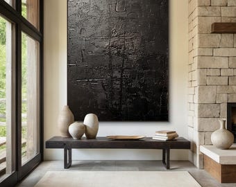 Puede incluir: Una gran pintura abstracta negra con una superficie texturizada cuelga de una pared sobre un banco de madera con tres jarrones de cerámica. La pintura está en una sala de estar moderna con una chimenea de piedra y una ventana grande.